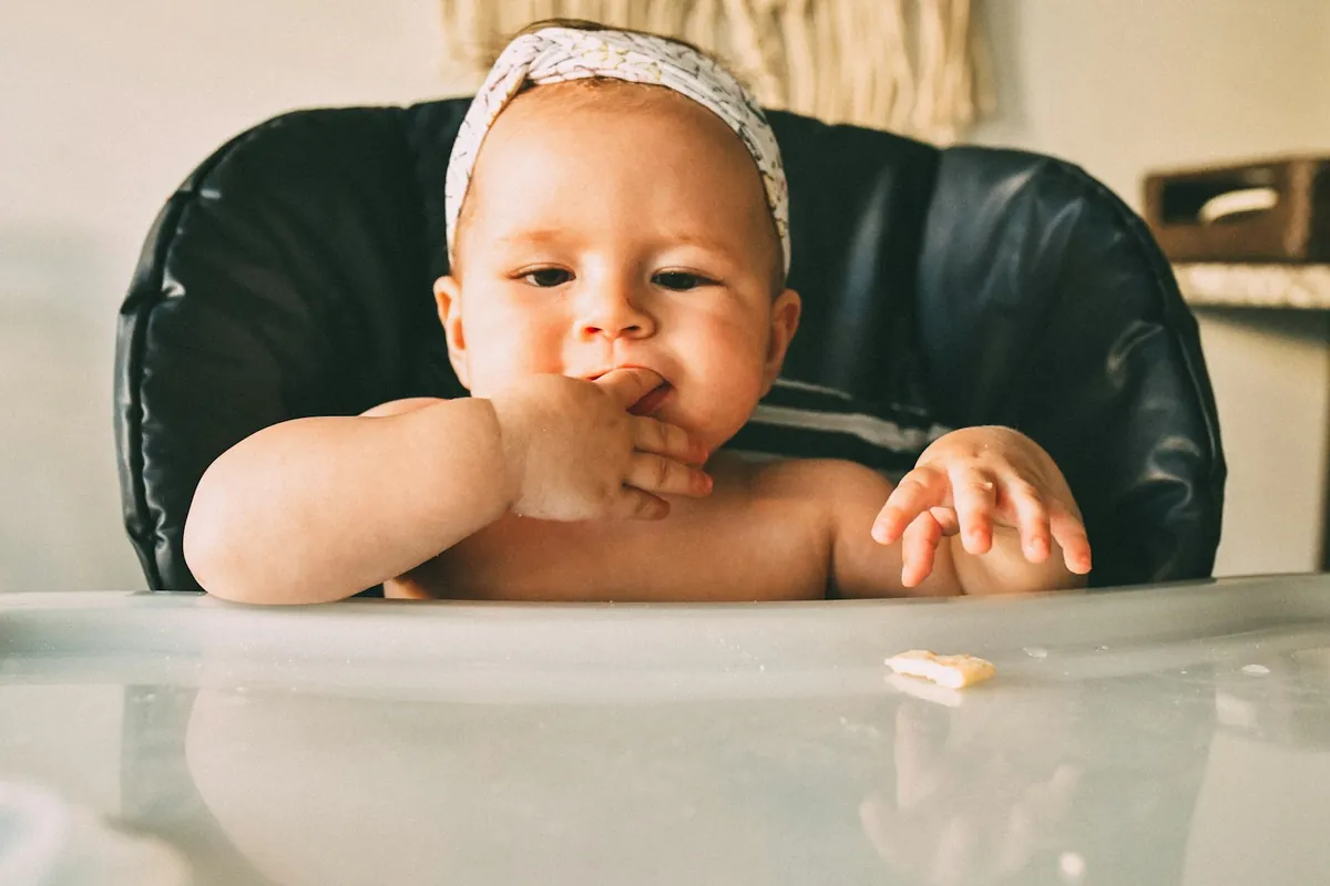 A baby eating with their hands in a high chair