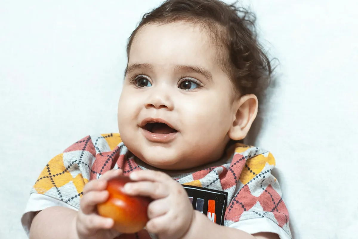 A baby holding a small tomato while sitting up