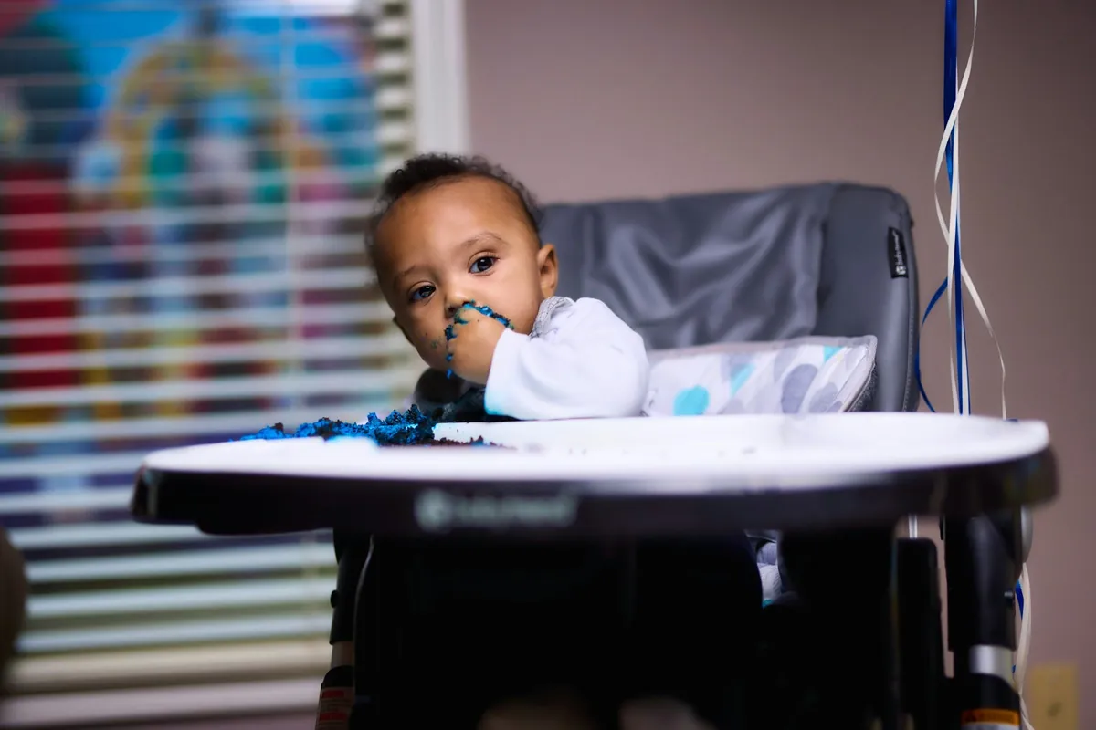 A baby sitting in a high chair beside a window