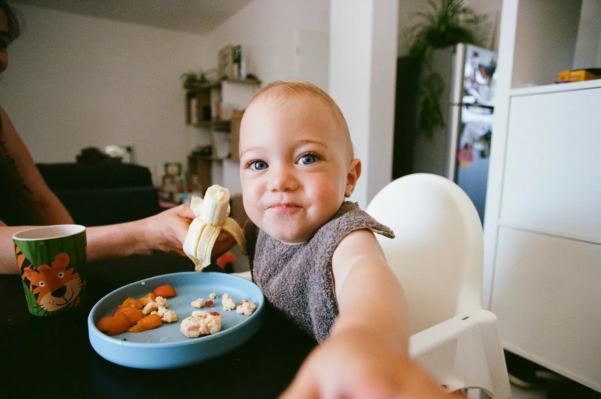 A baby in a high chair holding a piece of banana