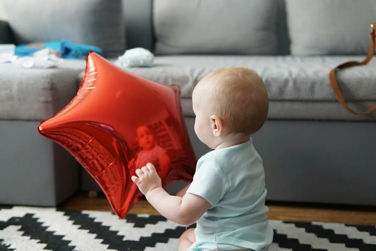A baby sitting on a rug playing with a foil balloon