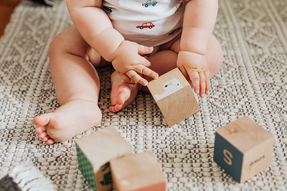 A baby sitting on a rug playing with wooden blocks