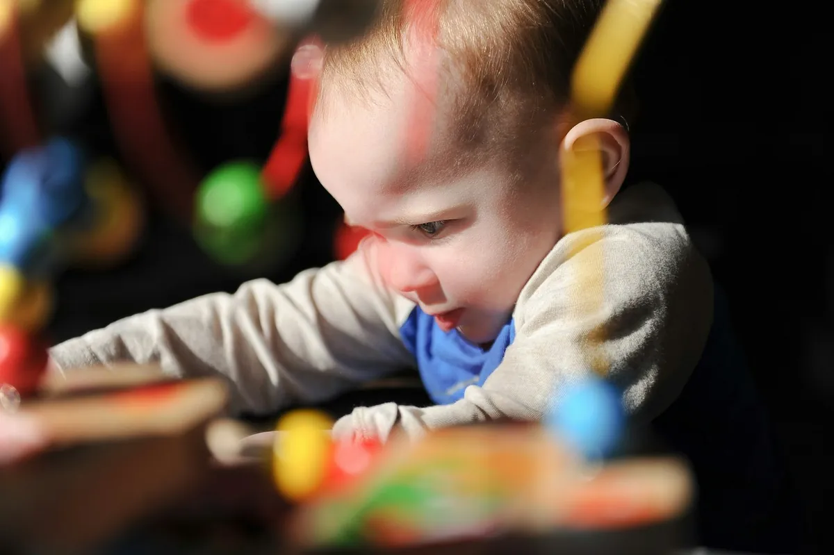 A baby reaching out for a wooden toy on the floor
