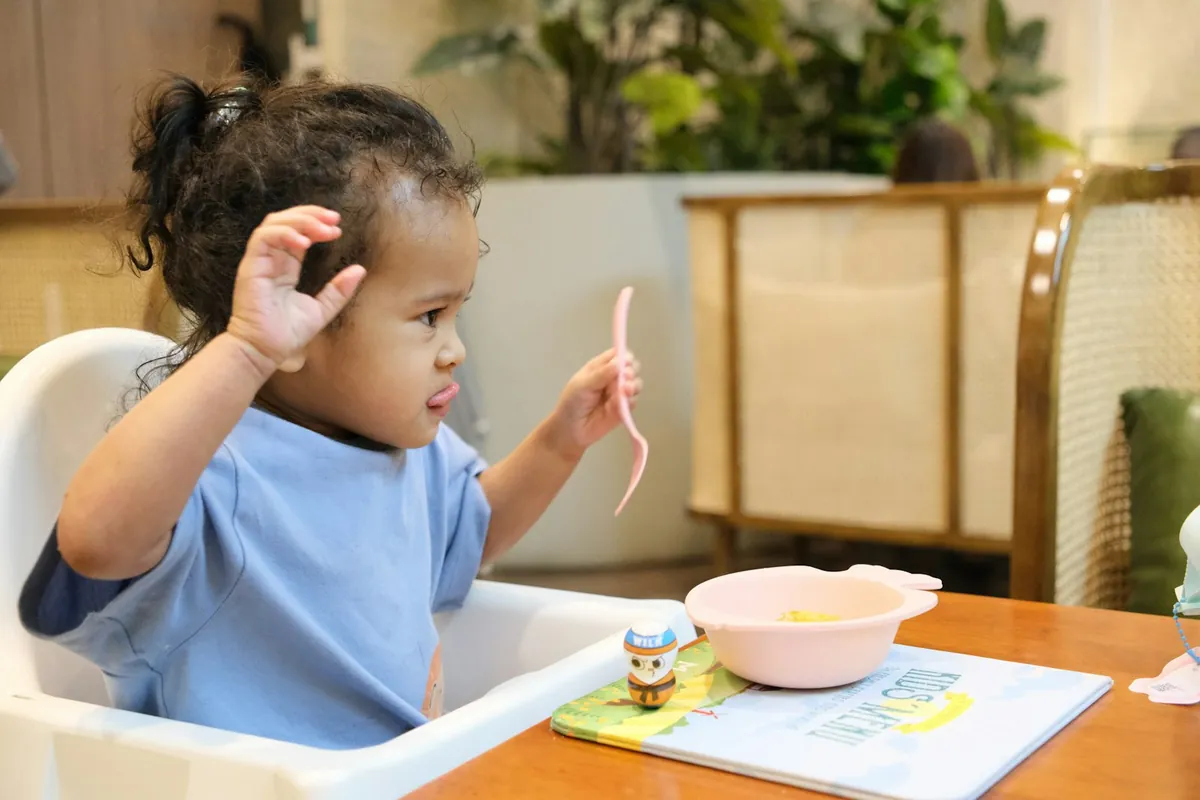 A baby in a high chair reaching towards food on a table