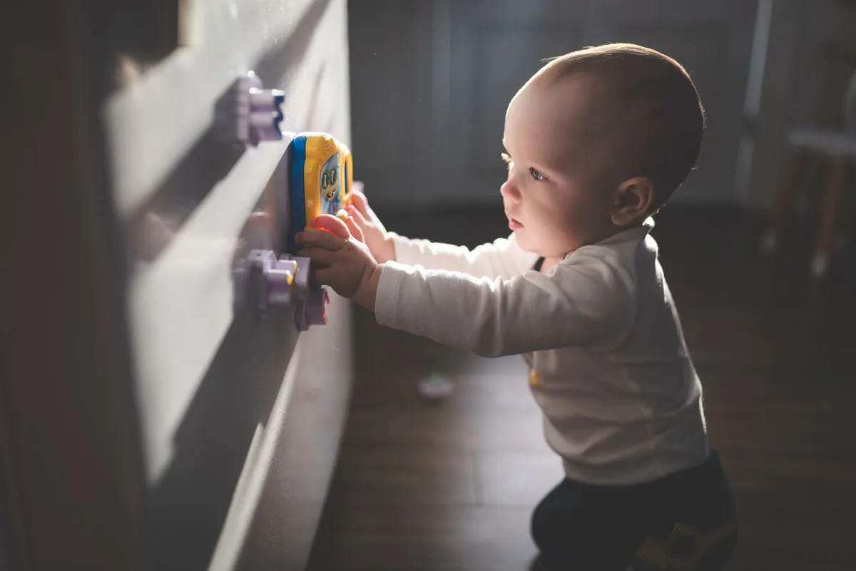 A baby standing and reaching up towards a toy