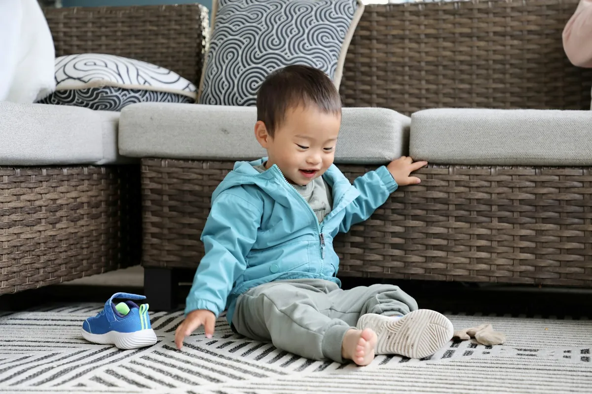 A baby sitting on a rug playing beside a sofa
