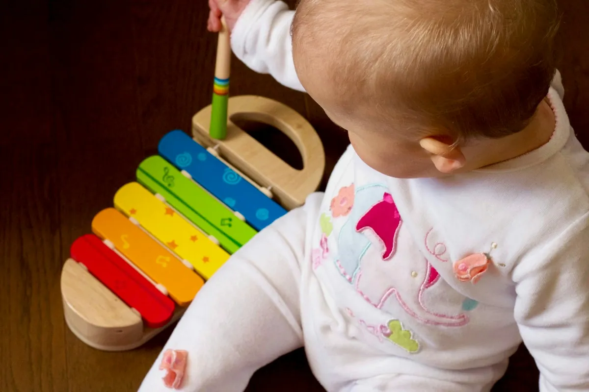 A baby reaching for a colourful wooden xylophone