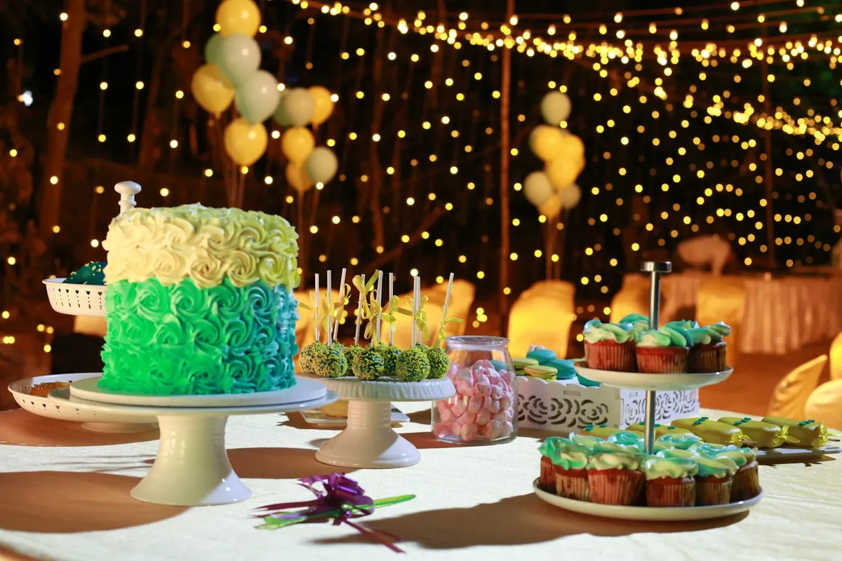 A green iced birthday cake beside cupcakes on a table
