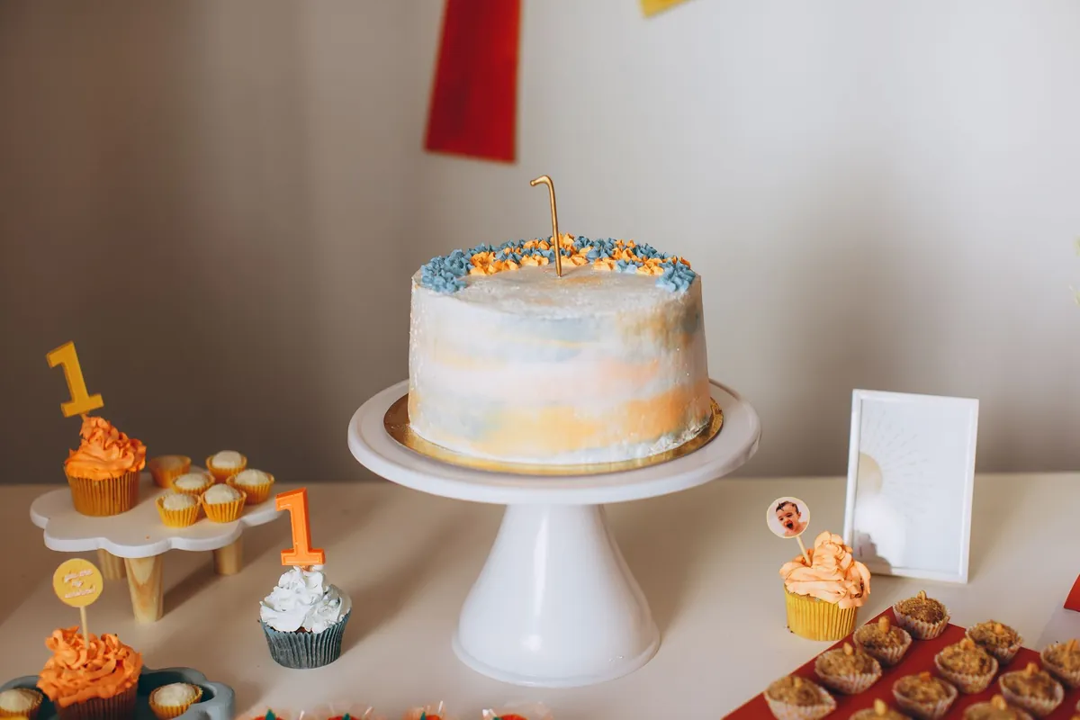 A birthday cake on a stand beside cupcakes on a table