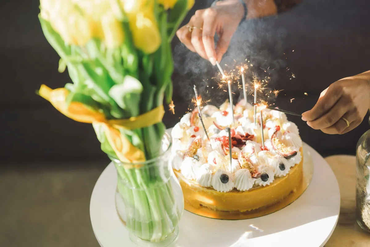 A birthday cake with lit candles beside a vase of tulips