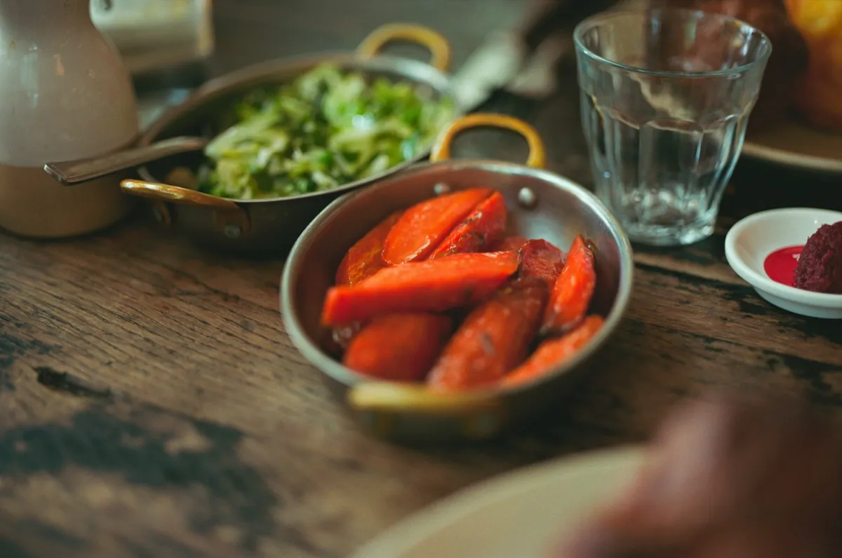 A bowl of cooked carrots on a wooden table