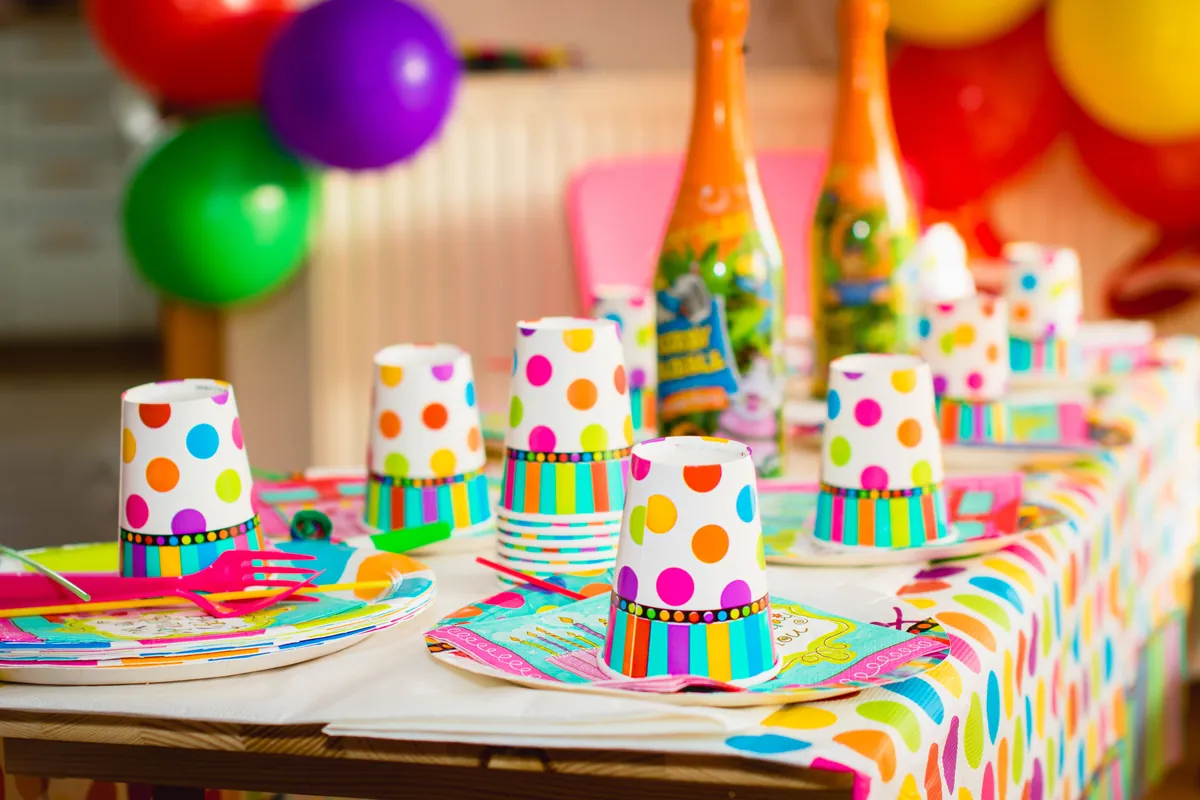 A brightly coloured party table set with cups and plates