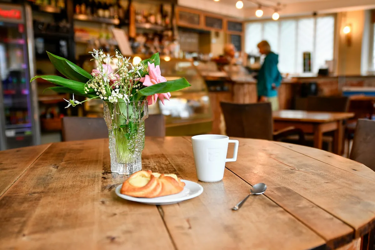 A cafe table with flowers, a pastry and a mug beside a window