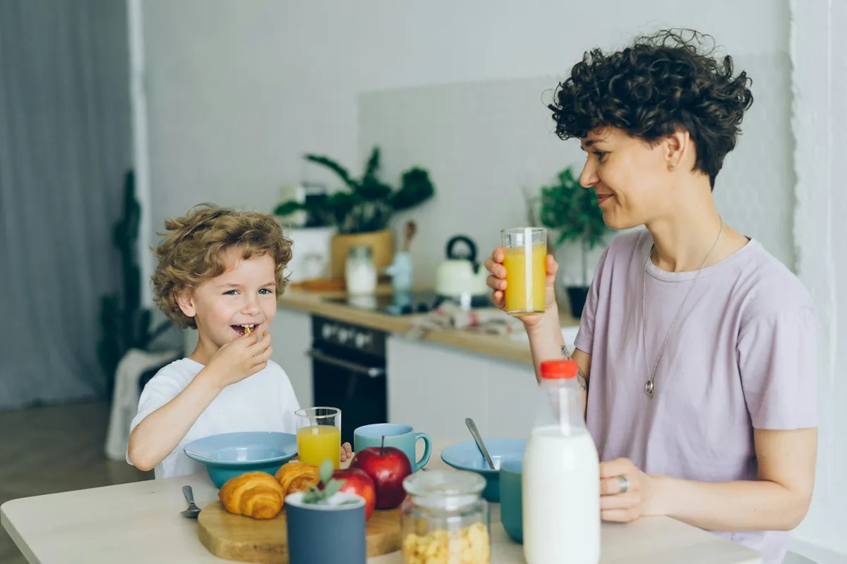 A child eating at a table while an adult stands nearby