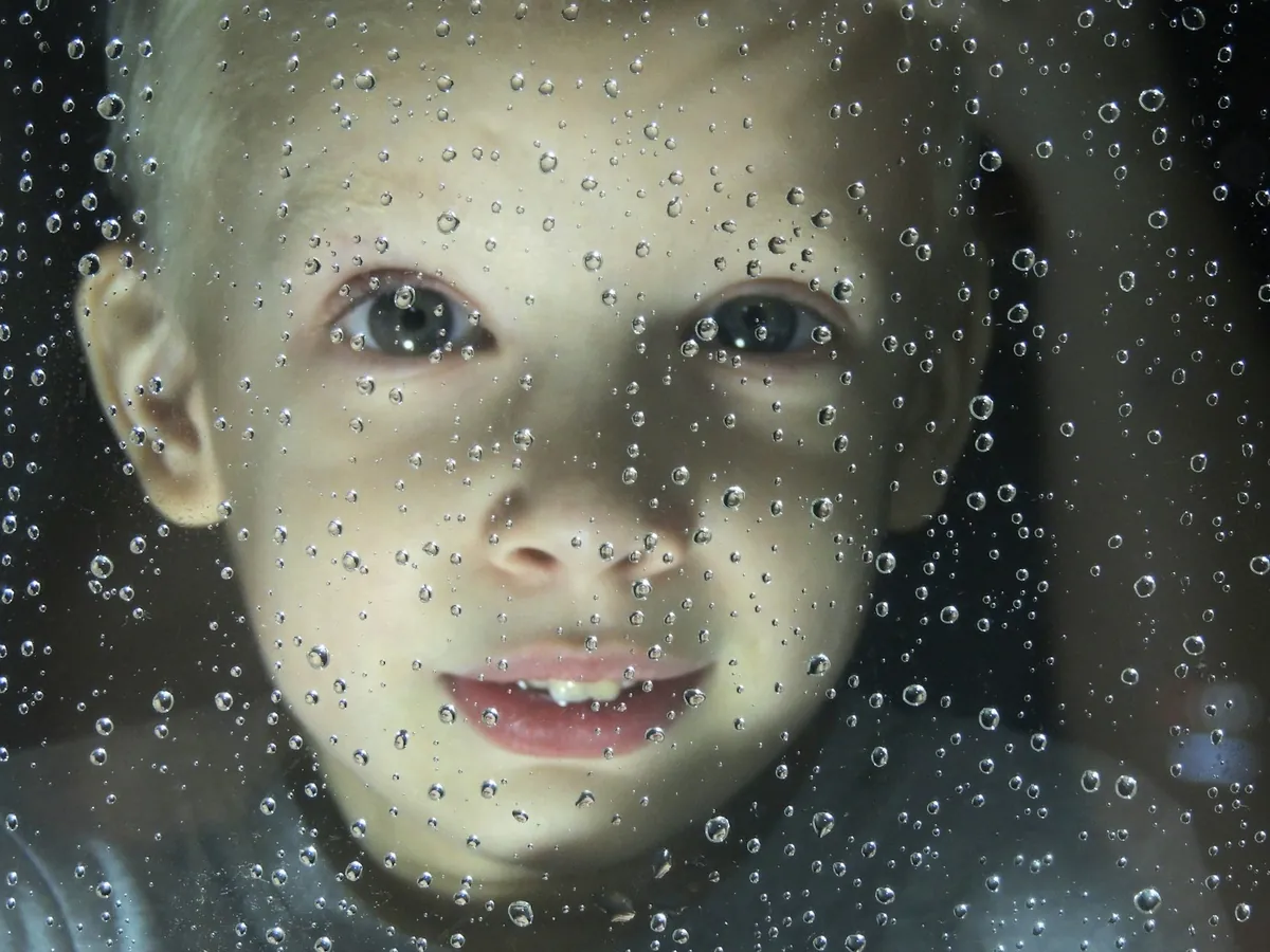 A child seen through a window covered in raindrops