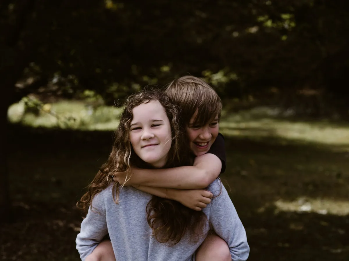 A child giving a younger sibling a piggyback outdoors