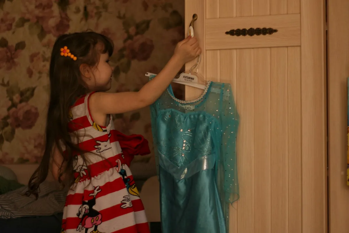 A young child reaching for a dressing-up outfit on a hanger