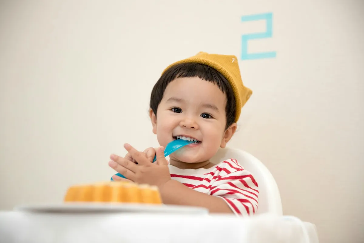 A young child in a paper hat eating with a spoon