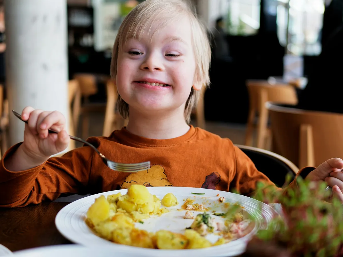 A young child smiling while eating a plated meal at a table