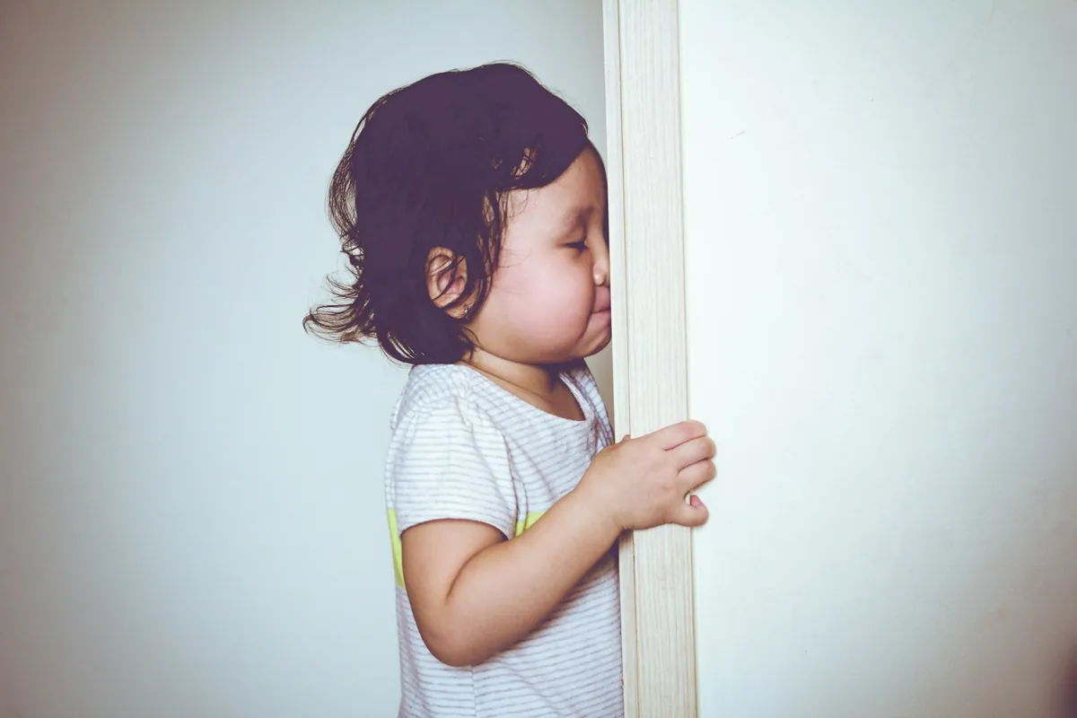A young child holding onto the edge of a doorframe