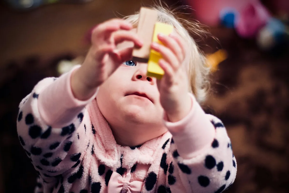 A young child holding wooden blocks up to their face
