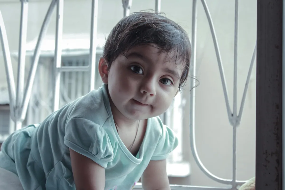 A young child looking out from an indoor play frame