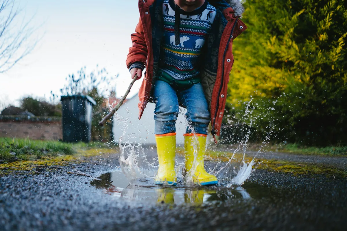 A child in yellow wellies jumping into a puddle