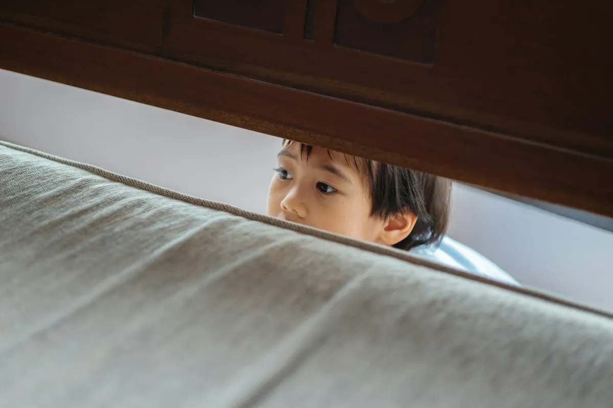 A young child looking out from behind a door