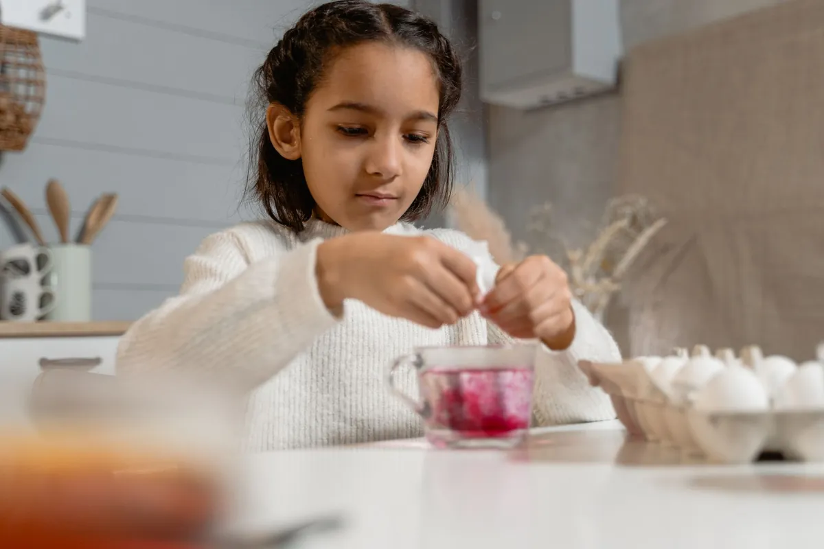 A child mixing coloured liquid in small cups at a table