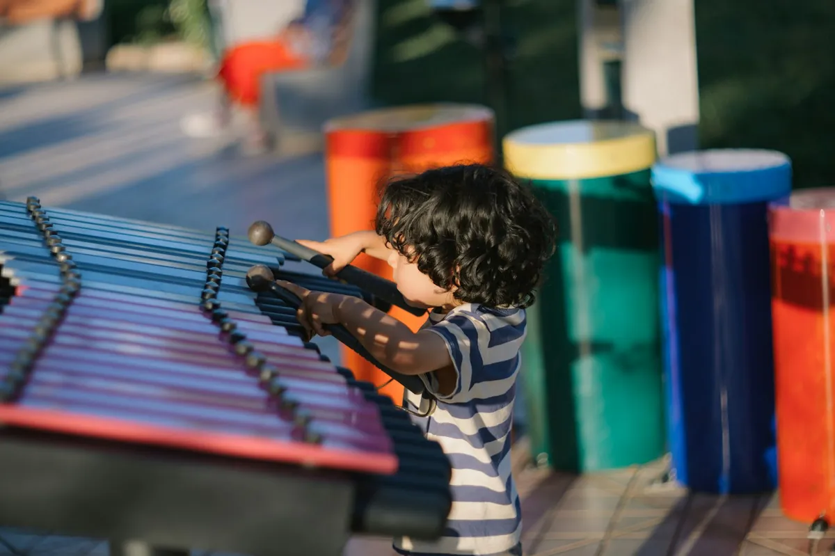 A young child playing a large outdoor xylophone