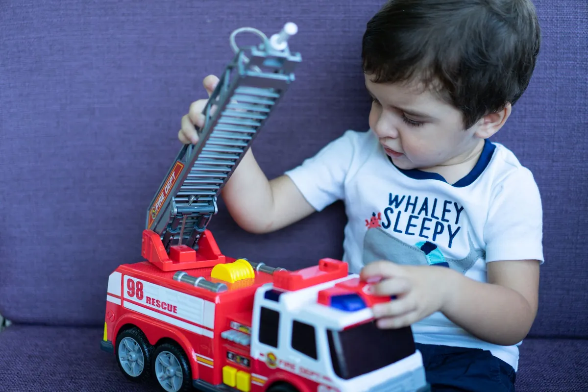 A young child playing with a red toy fire engine
