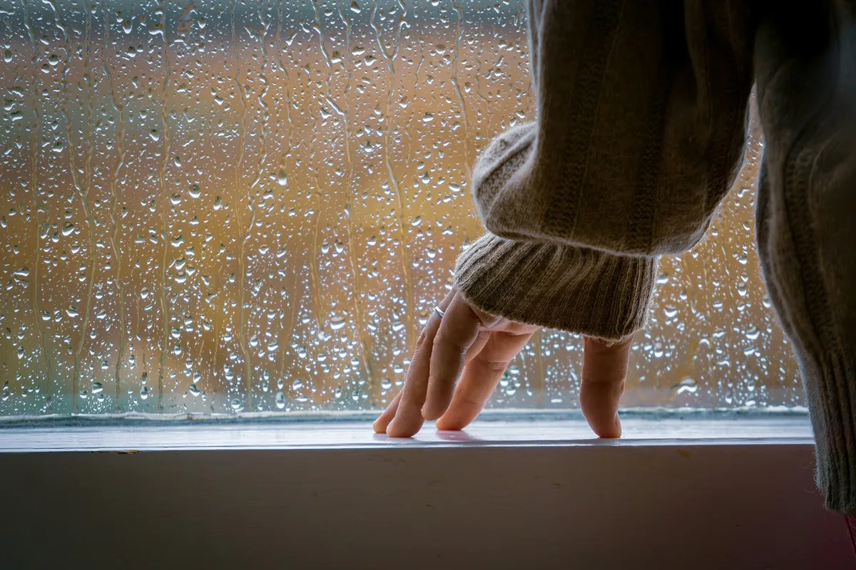 A child hand reaching towards a rain-covered window