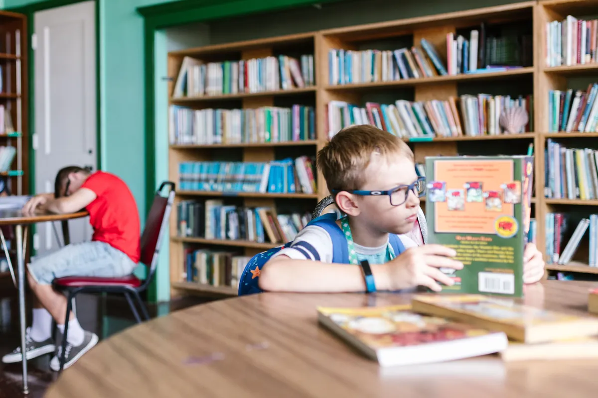 A child reading a book at a table in a library