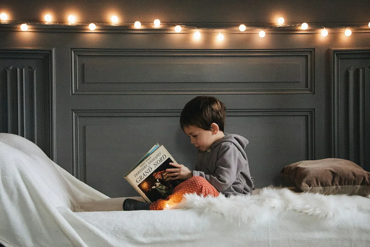 A child reading a book in a corner lit with string lights