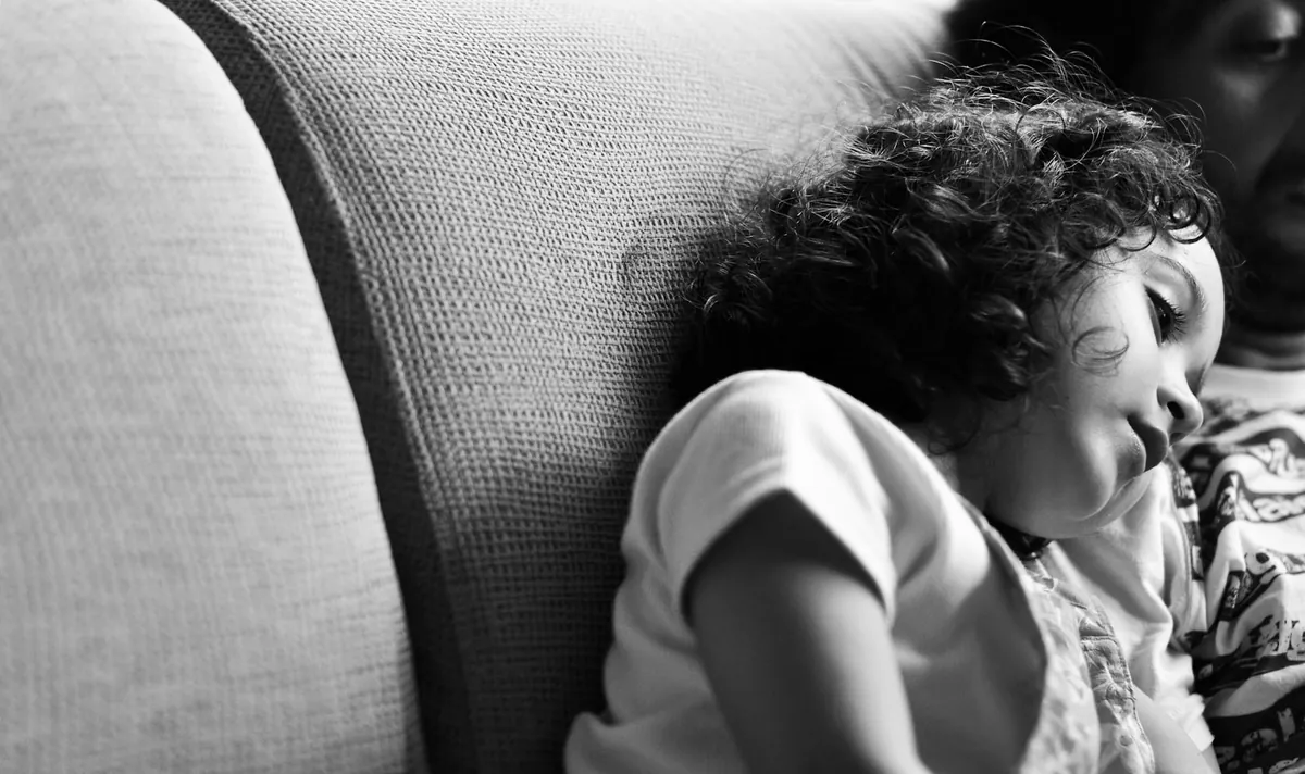 A child resting their head on a sofa cushion