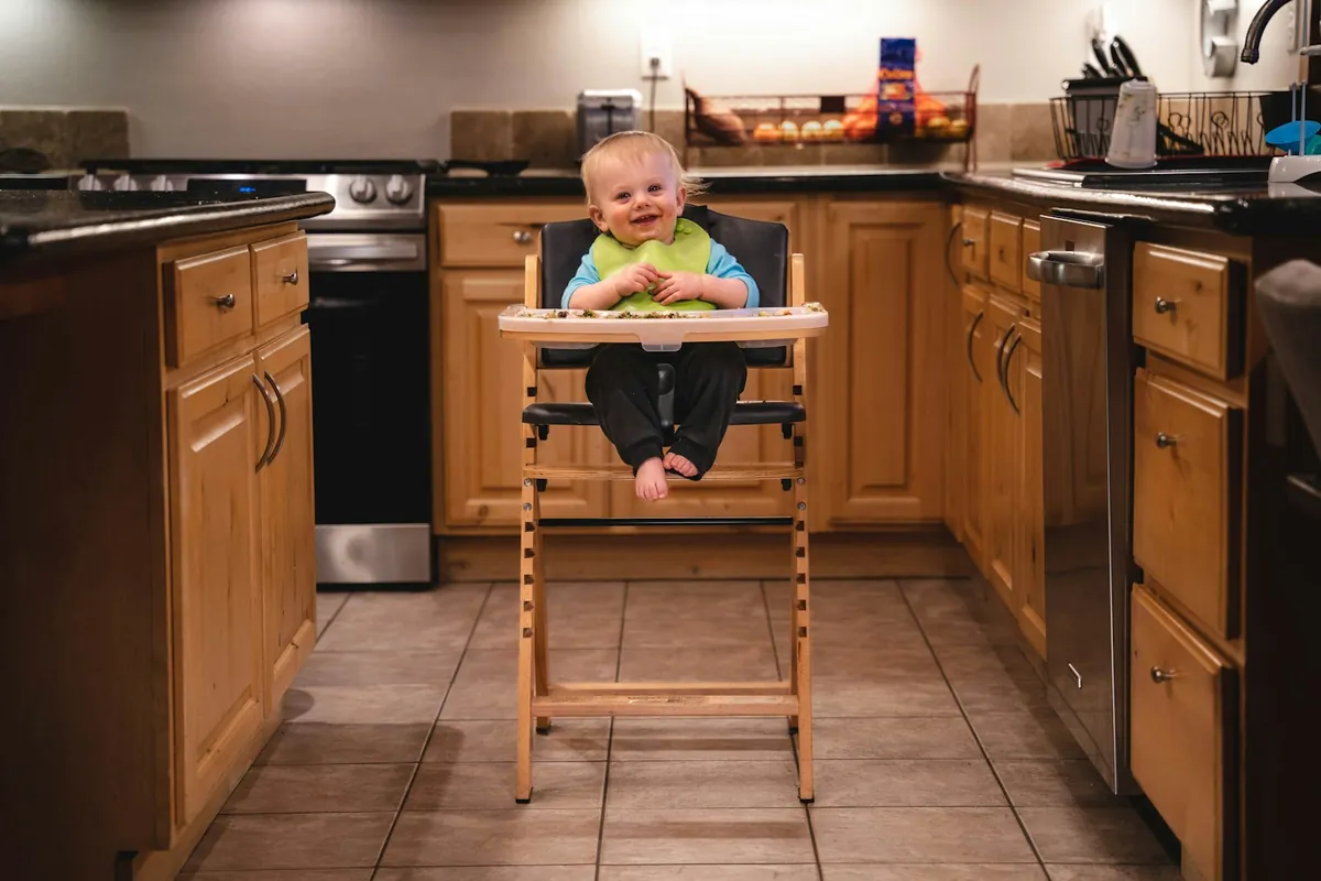 A child sitting in a tall wooden high chair in a kitchen