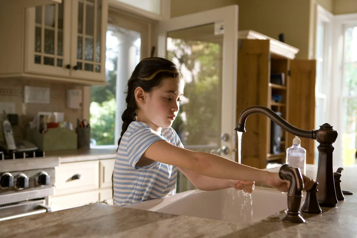 A child washing their hands at a kitchen tap