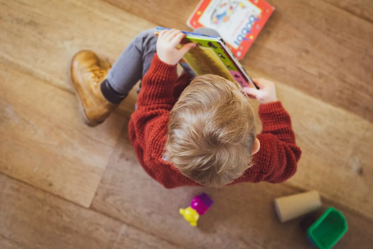 A child seen from above reading a book on the floor