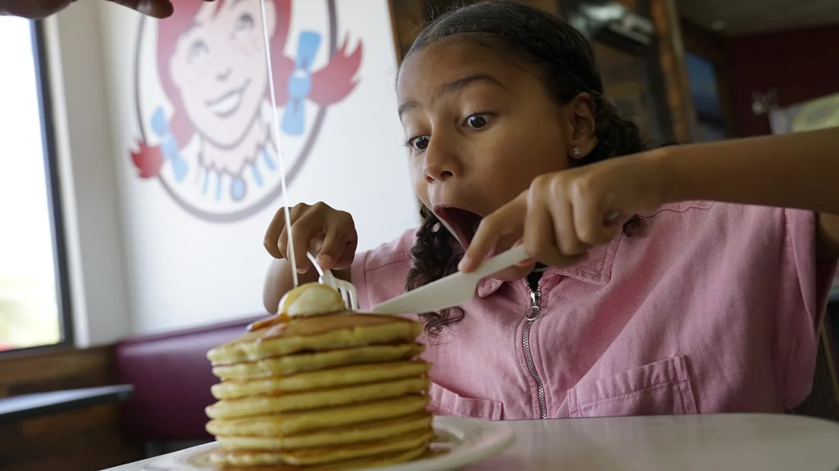 A child seated in a booth with a plate of pancakes