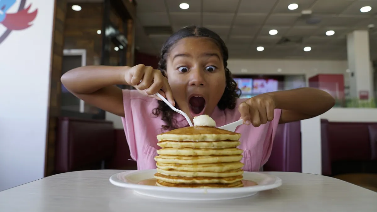 A child sitting in a booth with a tall stack of pancakes