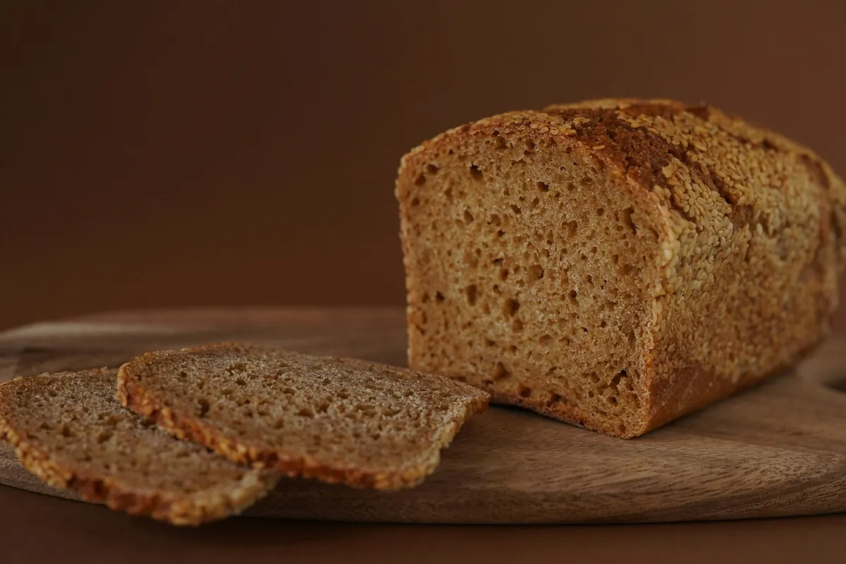 A dark loaf of bread, part sliced, on a board