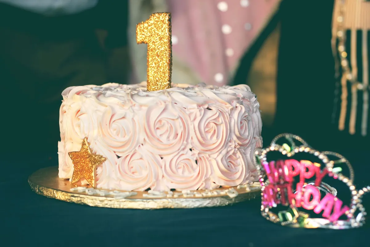 A pale iced birthday cake topped with a gold number one