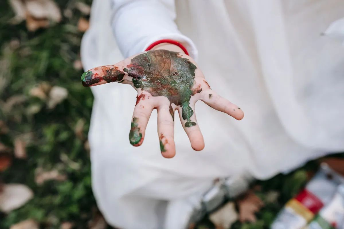 A child hand covered in blue and green paint