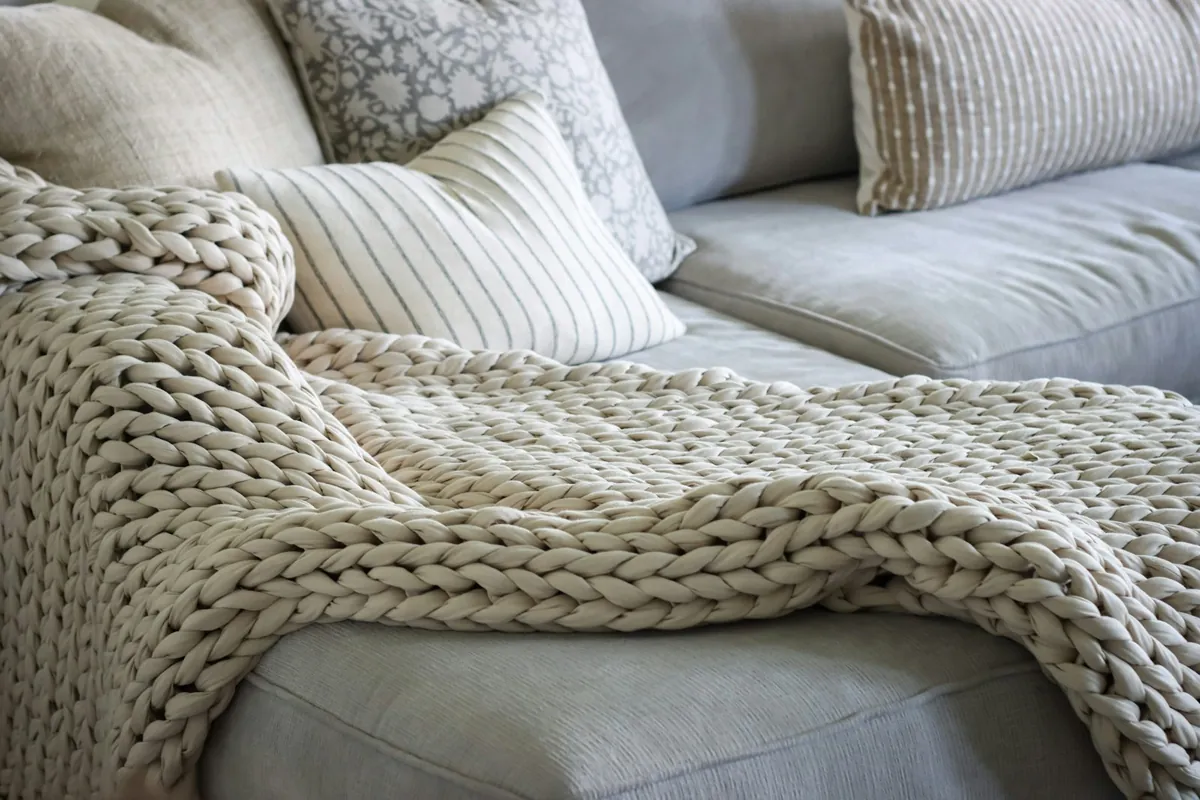 A knitted blanket and cushions on a sofa