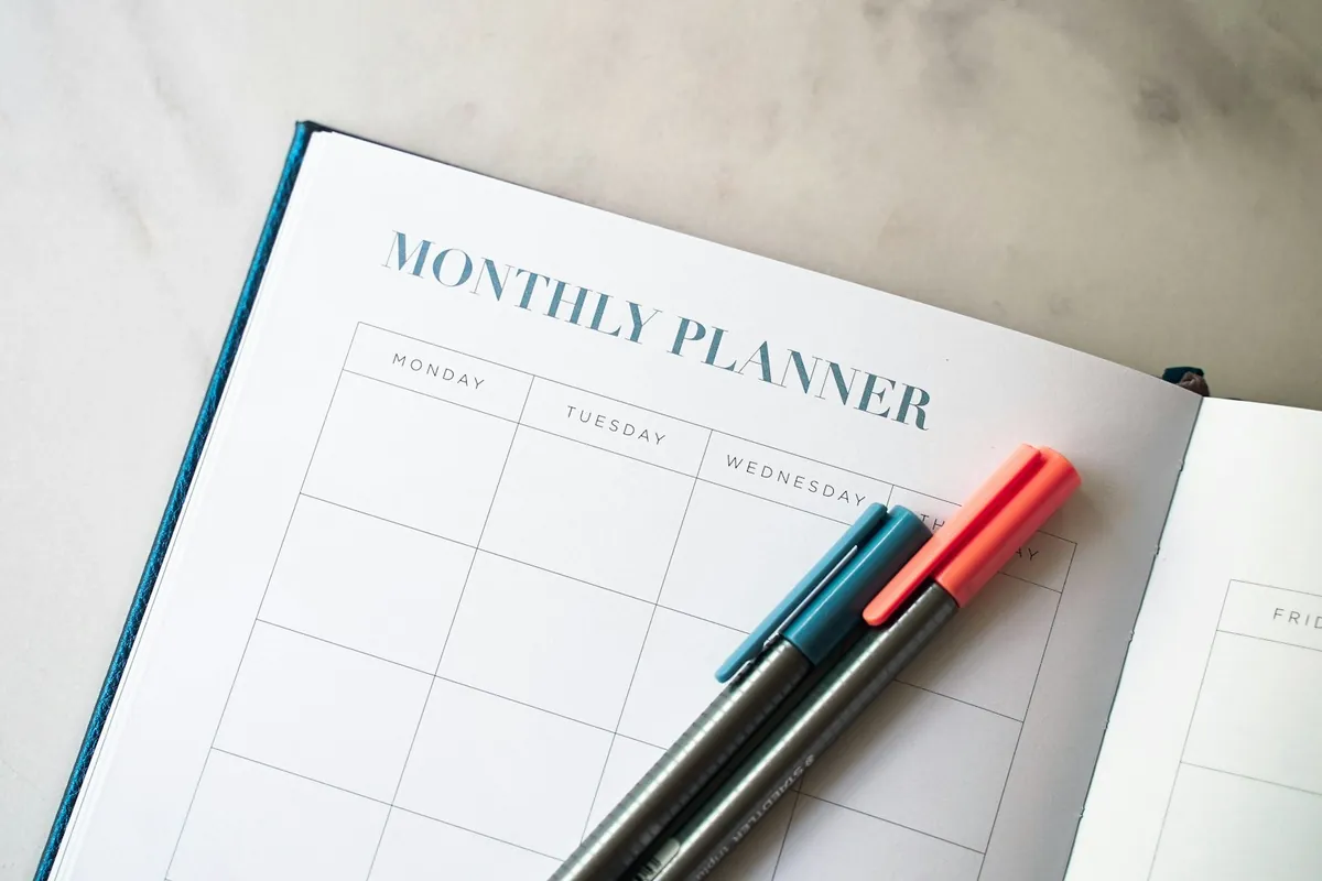 An open monthly planner with coloured pens beside it