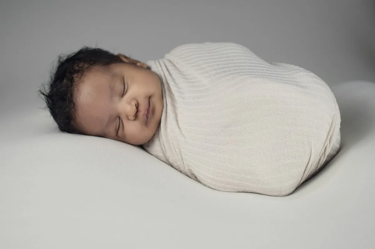 A newborn baby asleep wrapped in a white blanket