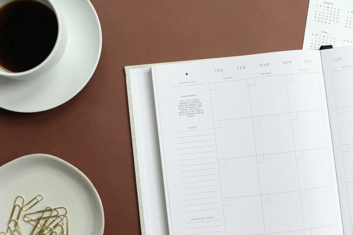 A notebook, coffee and paper clips arranged on a desk