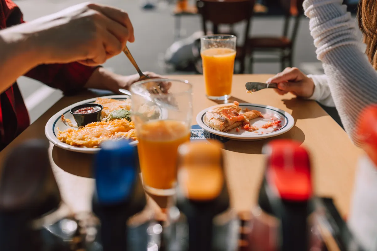 Hands reaching across a shared breakfast table of plates and drinks