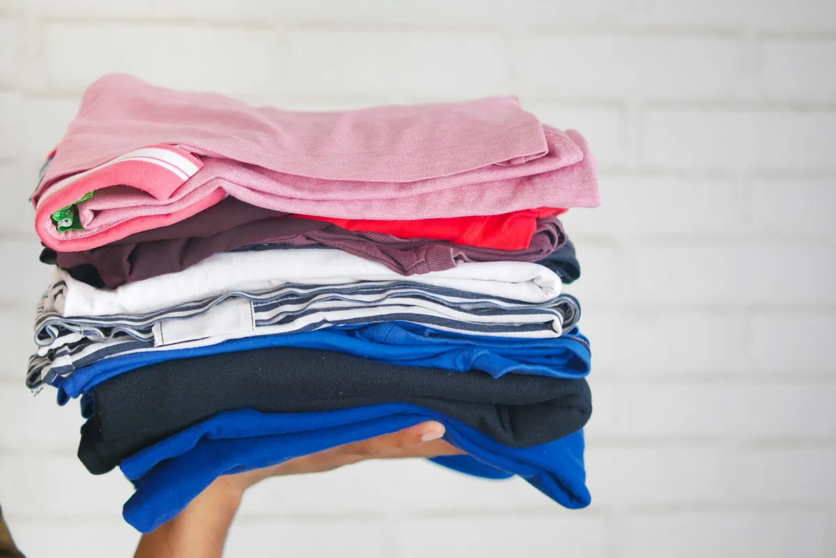 A stack of folded childrens clothes held in both hands