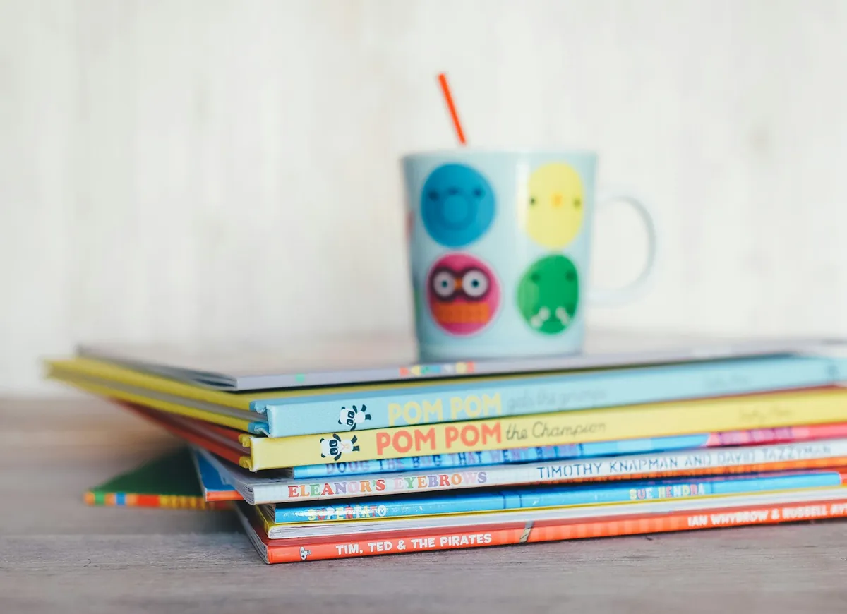 A stack of picture books beside a child cup